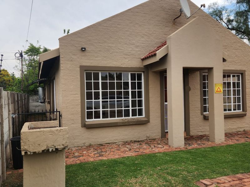 Front exterior view of a single-story apartment featuring a paved walkway, built-in braai, and secure boundary wall.