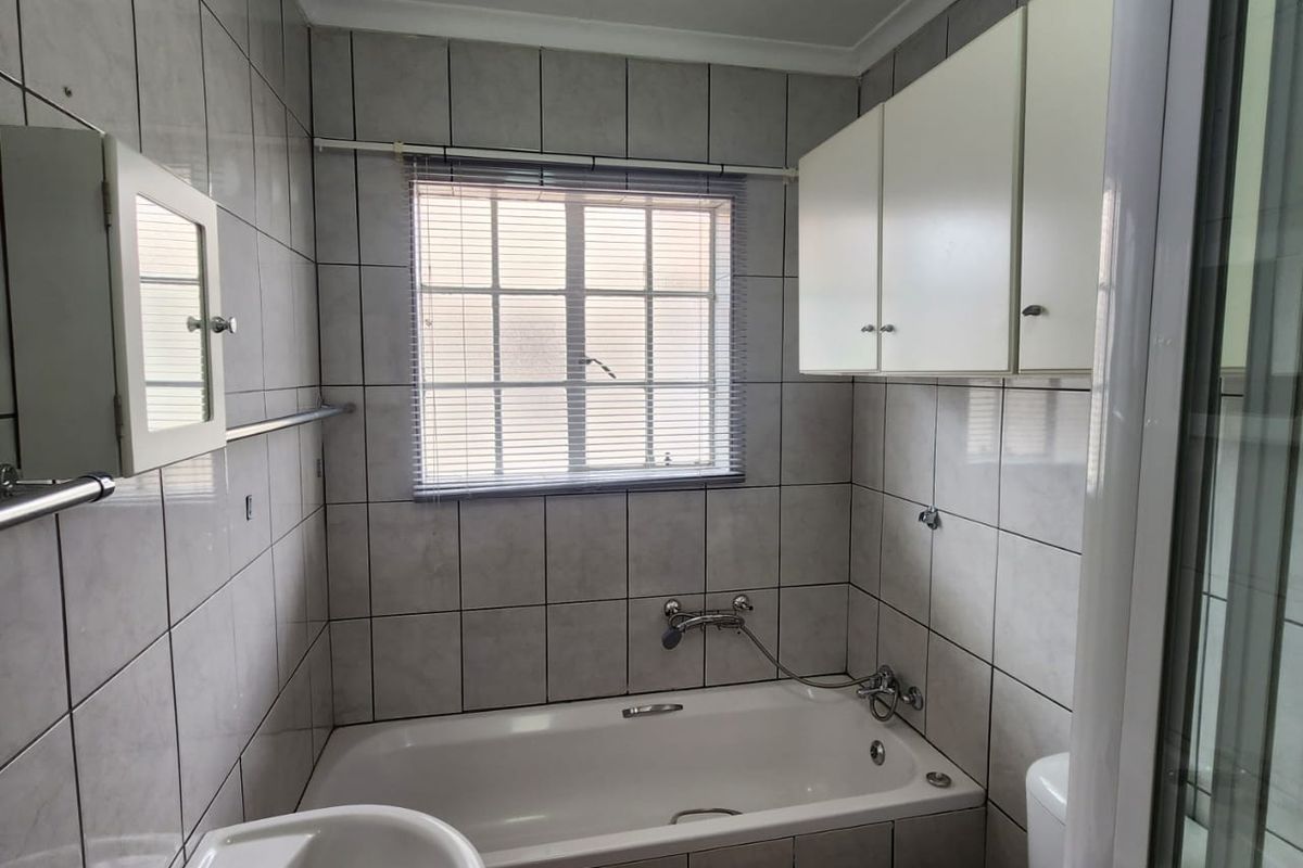 A functional bathroom featuring a bathtub, wall-mounted basin, toilet, and overhead cabinetry, finished with neutral wall tiles.