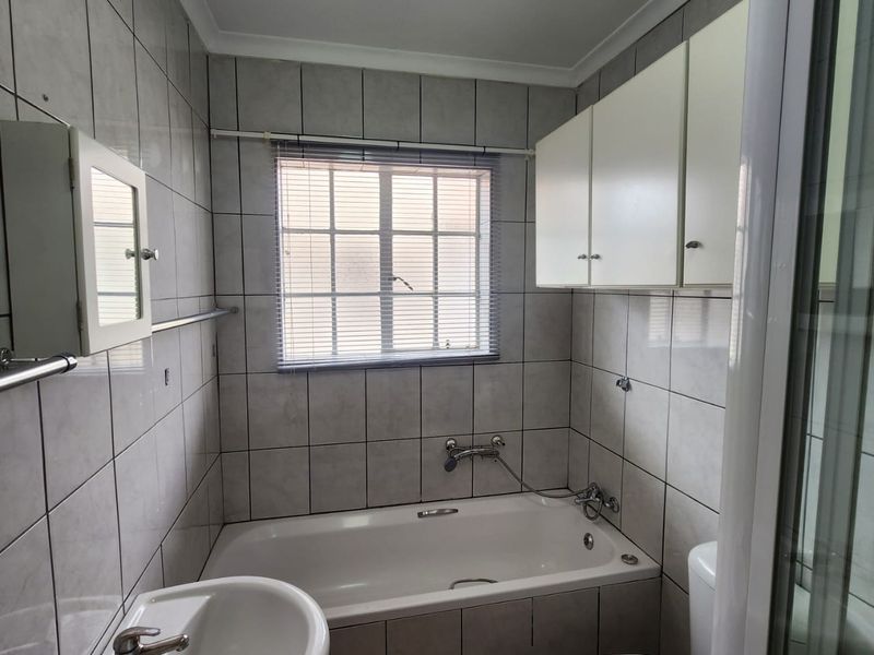 A functional bathroom featuring a bathtub, wall-mounted basin, toilet, and overhead cabinetry, finished with neutral wall tiles.