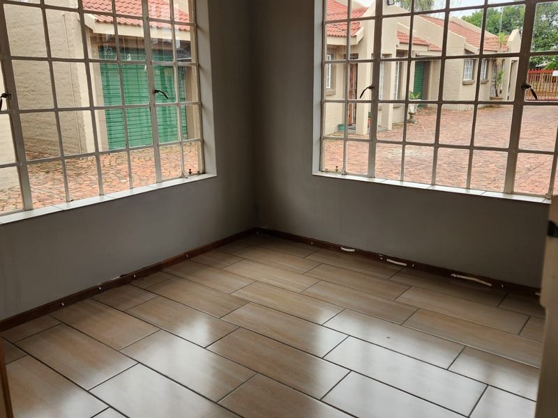 An empty living area featuring large grid-pattern windows and tiled flooring, offering a bright and neutral space ready for personalization.