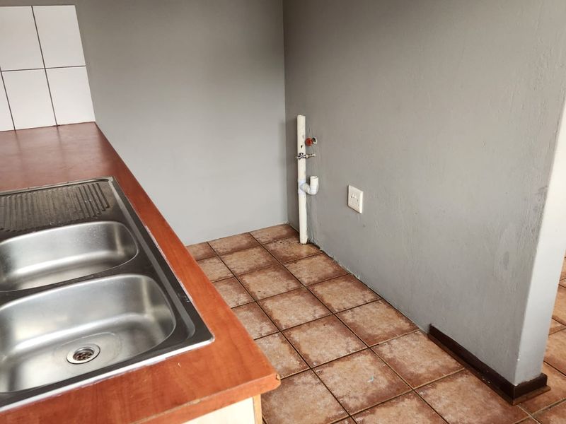 A functional kitchen area featuring a stainless steel double sink, laminate countertop, and tiled flooring with exposed plumbing connections.