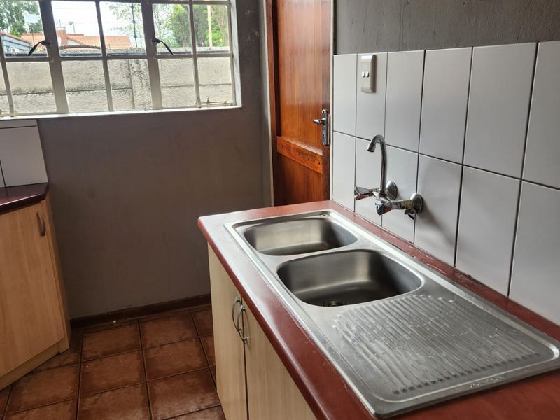 A functional kitchen area featuring a double stainless steel sink, tiled splashback, laminate countertops, and built-in cabinetry with tiled flooring.