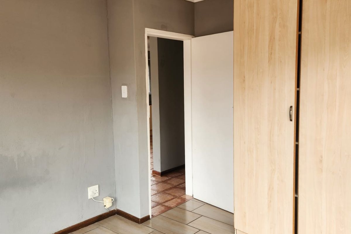 An empty bedroom featuring tiled flooring, a built-in wooden wardrobe, and neutral grey walls with access to an adjoining hallway.