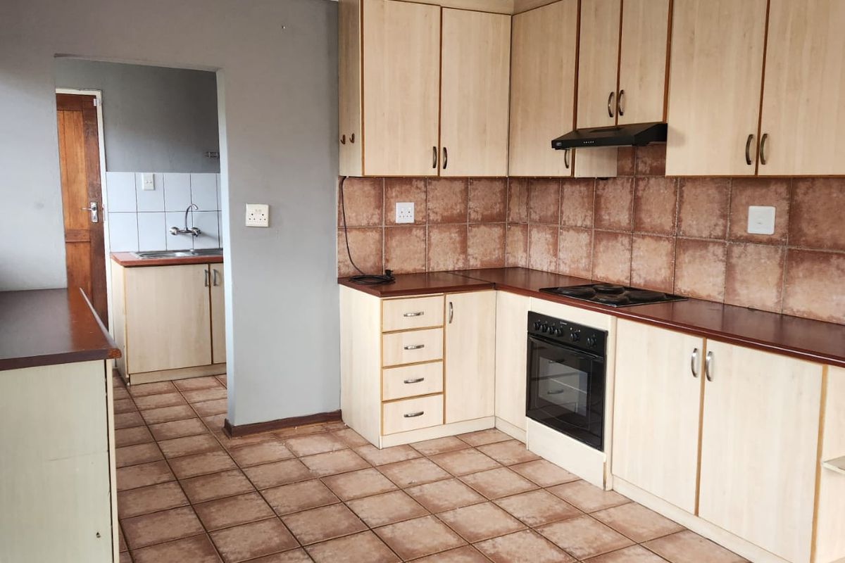 A functional kitchen featuring built-in cabinetry, laminate countertops, and a tiled backsplash, with an adjoining scullery area and tiled flooring throughout.