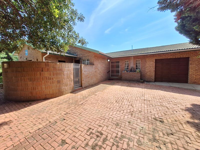Front exterior view of a brick house featuring a paved driveway, attached garage, and secure entrance gate.