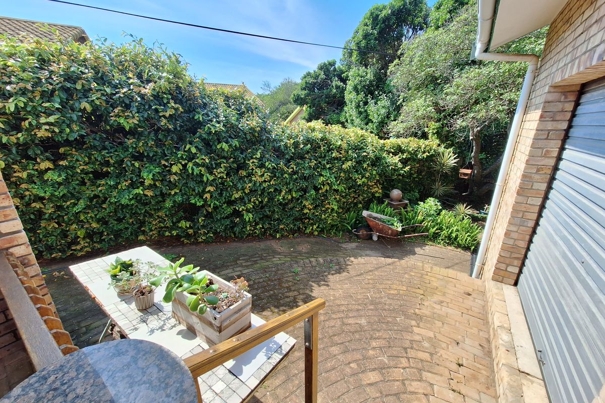 A private rear courtyard featuring brick paving, established hedge screening, and direct access to the garage area.