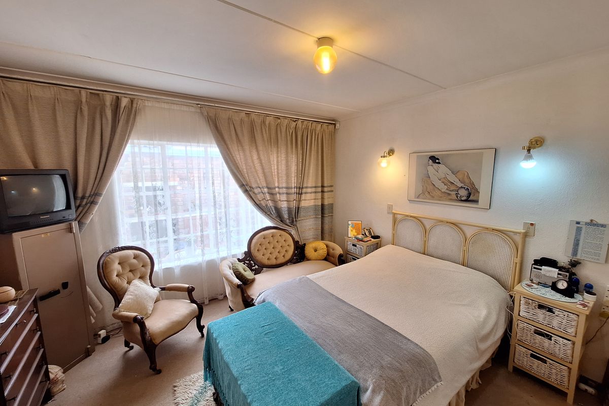 A carpeted bedroom featuring large windows with curtains and wall-mounted lighting fixtures.