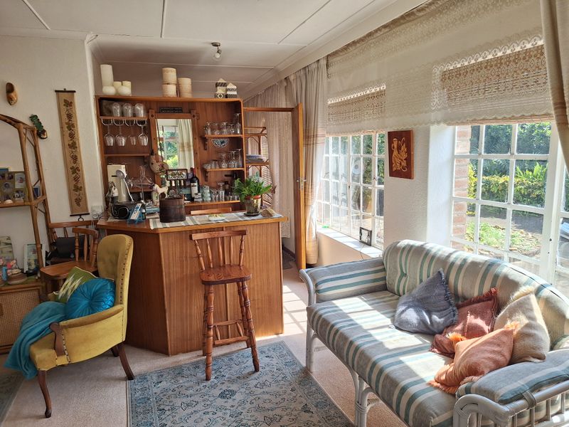 A living room area featuring a built-in wooden bar unit and large multi-pane windows that provide natural light and garden views.