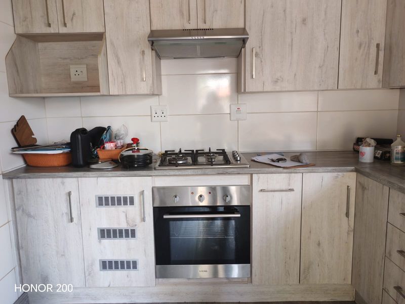 A functional kitchen featuring light wood-grain cabinetry, a built-in gas hob, an oven, and a tiled splashback with ample counter space.