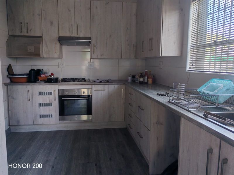 A functional kitchen featuring light wood-grain cabinetry, a built-in gas hob, electric oven, and a stainless steel sink with ample counter space.