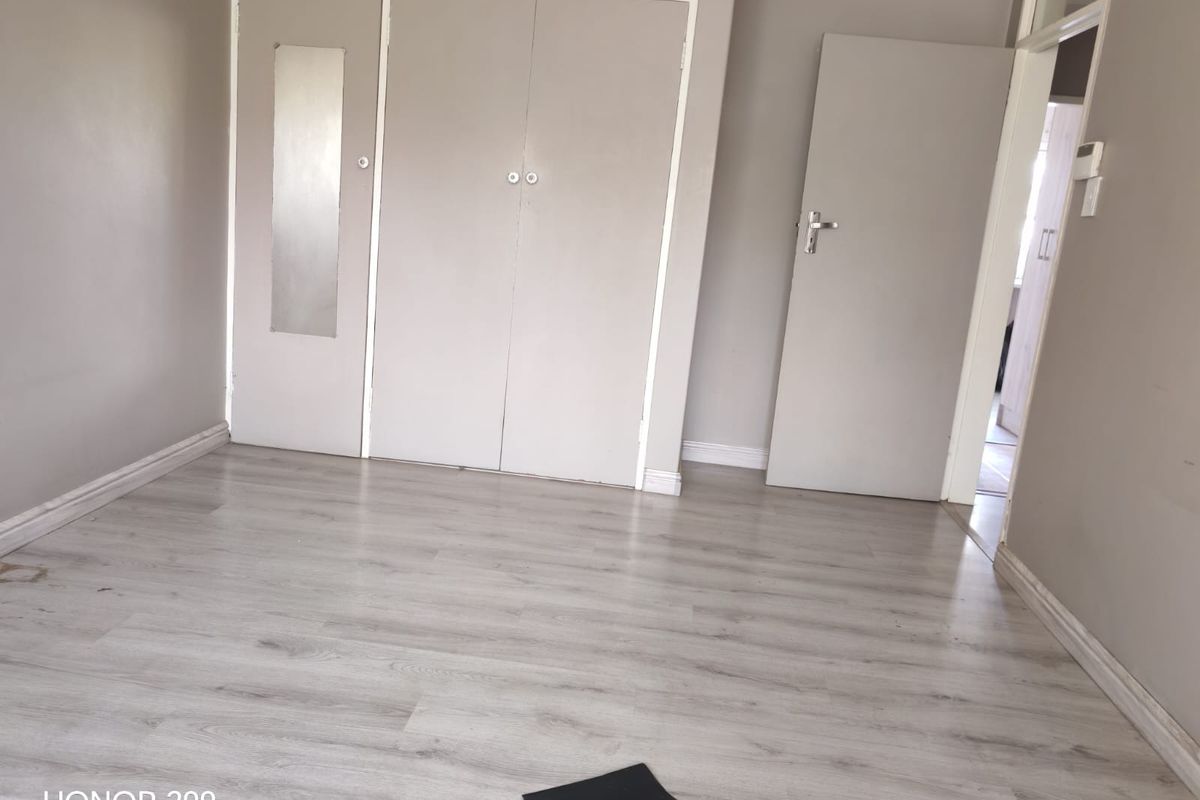 A clean, empty bedroom featuring light-toned laminate flooring and built-in cupboards, offering a neutral canvas for personalization.