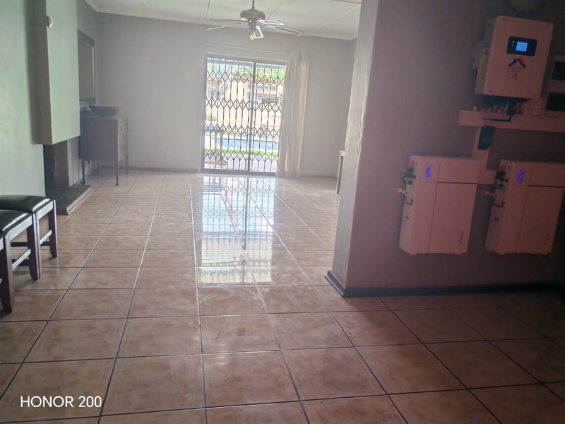 Spacious living area featuring tiled floors, a fireplace, and a wall-mounted solar power system with battery storage, leading to an outdoor patio area.