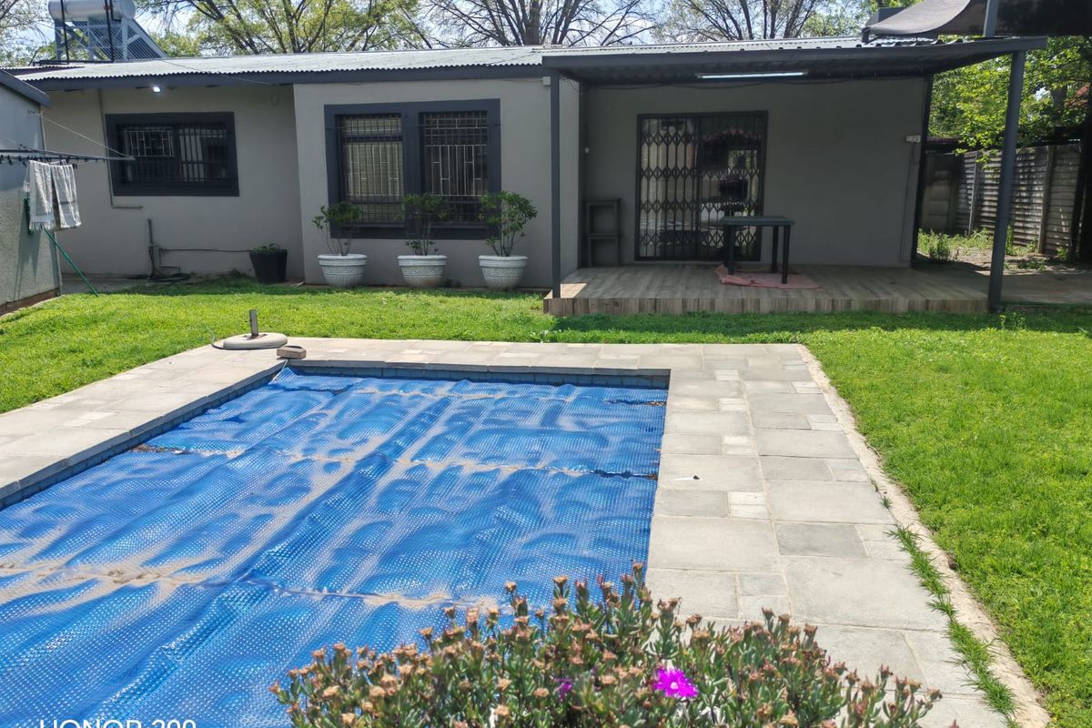 Rear view of the property featuring a swimming pool with cover, a covered patio area, and a well-maintained garden space.