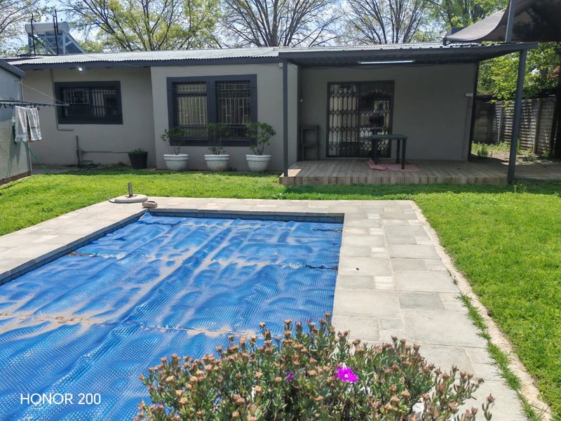 Rear view of the property featuring a swimming pool with cover, a covered patio area, and a well-maintained garden space.