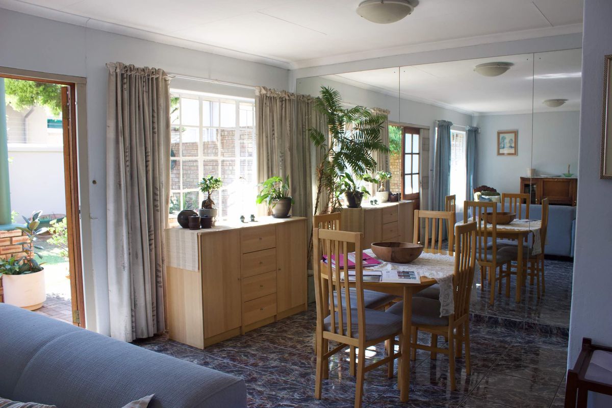 Living and dining area featuring tiled flooring, a large mirrored wall, and direct access to the garden through a glass-paneled door.