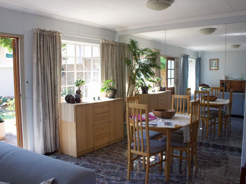 Living and dining area featuring tiled flooring, a large mirrored wall, and direct access to the garden through a glass-paneled door.