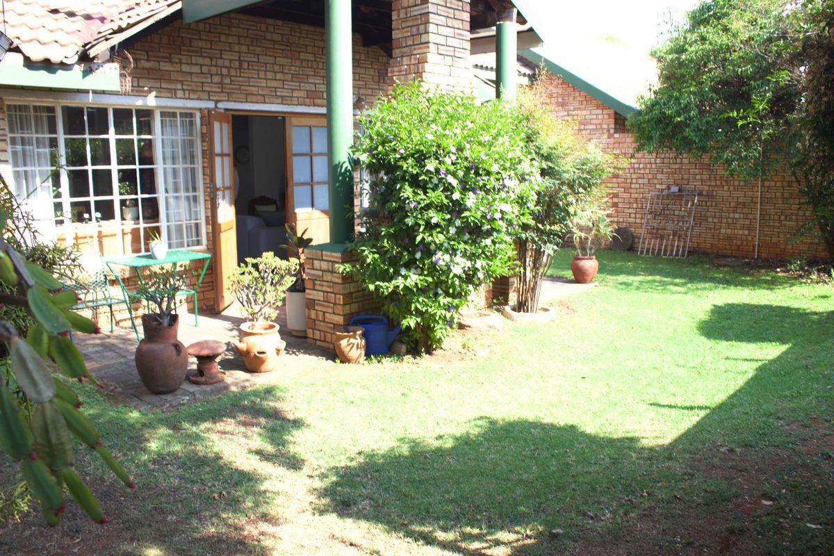 A rear view of the townhouse featuring a covered patio area, brick facade, and a private garden with a lawn.