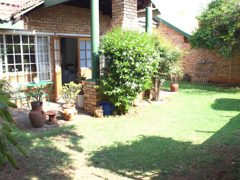 A rear view of the townhouse featuring a covered patio area, brick facade, and a private garden with a lawn.
