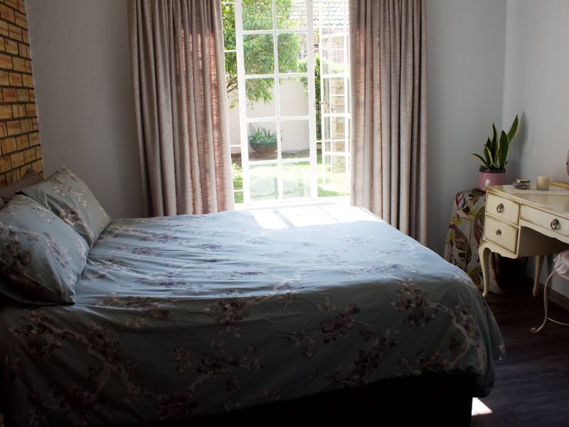 Bedroom featuring an exposed brick accent wall, dark laminate flooring, and French doors providing direct access to the garden.