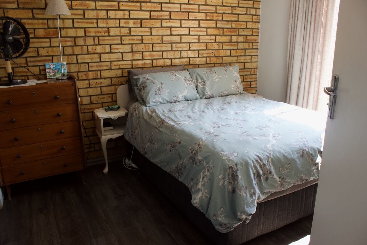 A bedroom featuring an exposed brick feature wall and dark laminate flooring, providing a rustic aesthetic with natural light from the window.