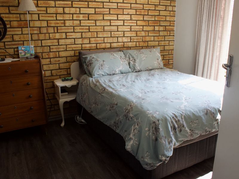 A bedroom featuring an exposed brick feature wall and dark laminate flooring, providing a rustic aesthetic with natural light from the window.