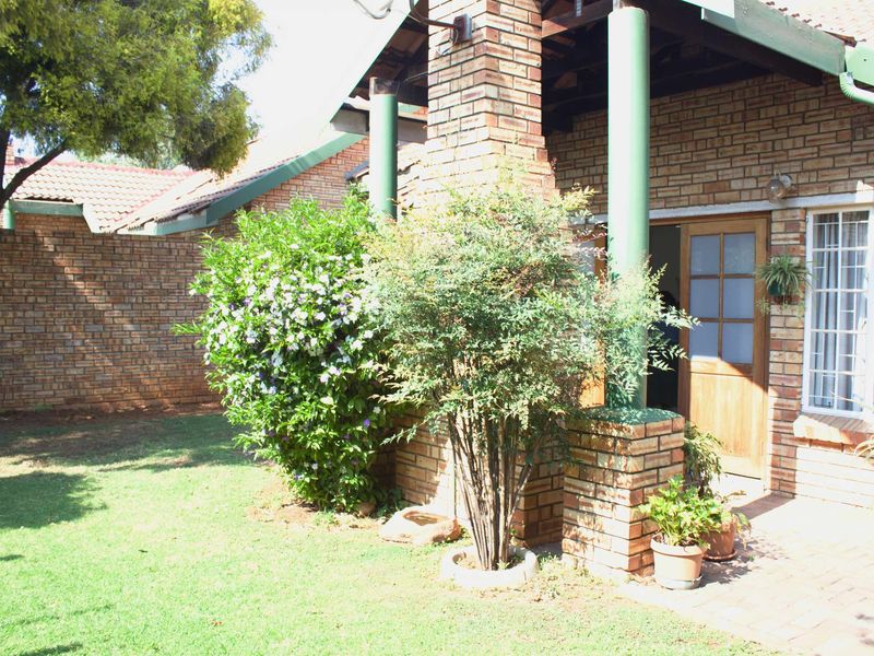 Rear view of the townhouse featuring a brick facade, covered patio area, and a well-maintained garden space.