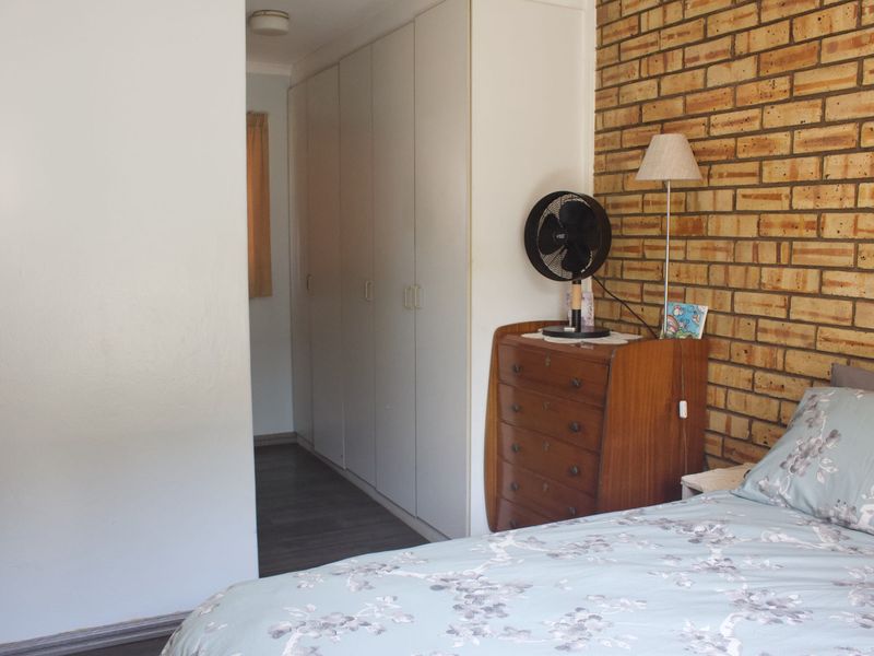 A bedroom featuring an exposed brick feature wall, laminate flooring, and built-in cupboards providing ample storage space.