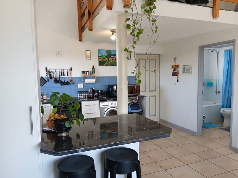Open-plan kitchen and living area featuring a stone breakfast bar, tiled backsplash, and access to a mezzanine level and adjacent bathroom.