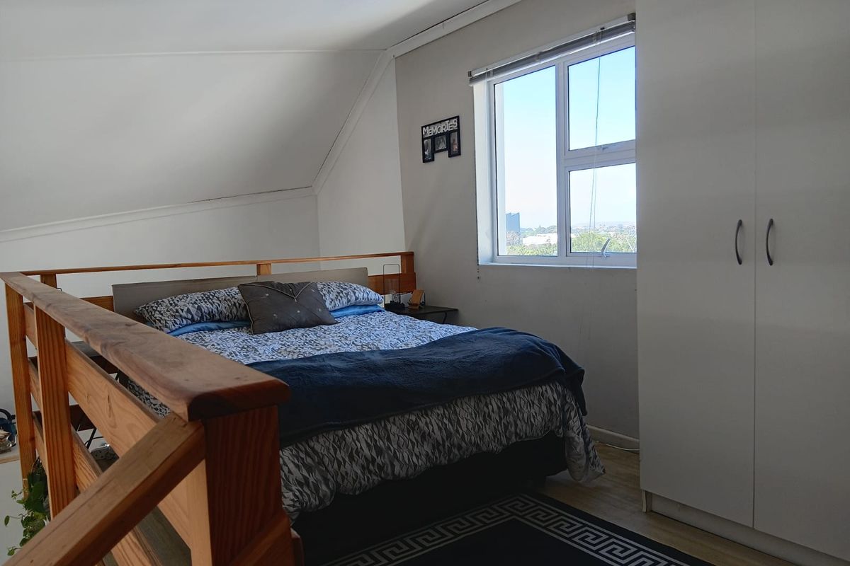 Loft-style bedroom featuring a built-in wardrobe, timber balustrade, and large window providing natural light and elevated views.