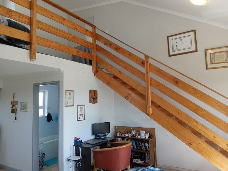 Living area featuring a wooden staircase leading to a mezzanine level, with built-in storage and access to an adjacent bathroom.