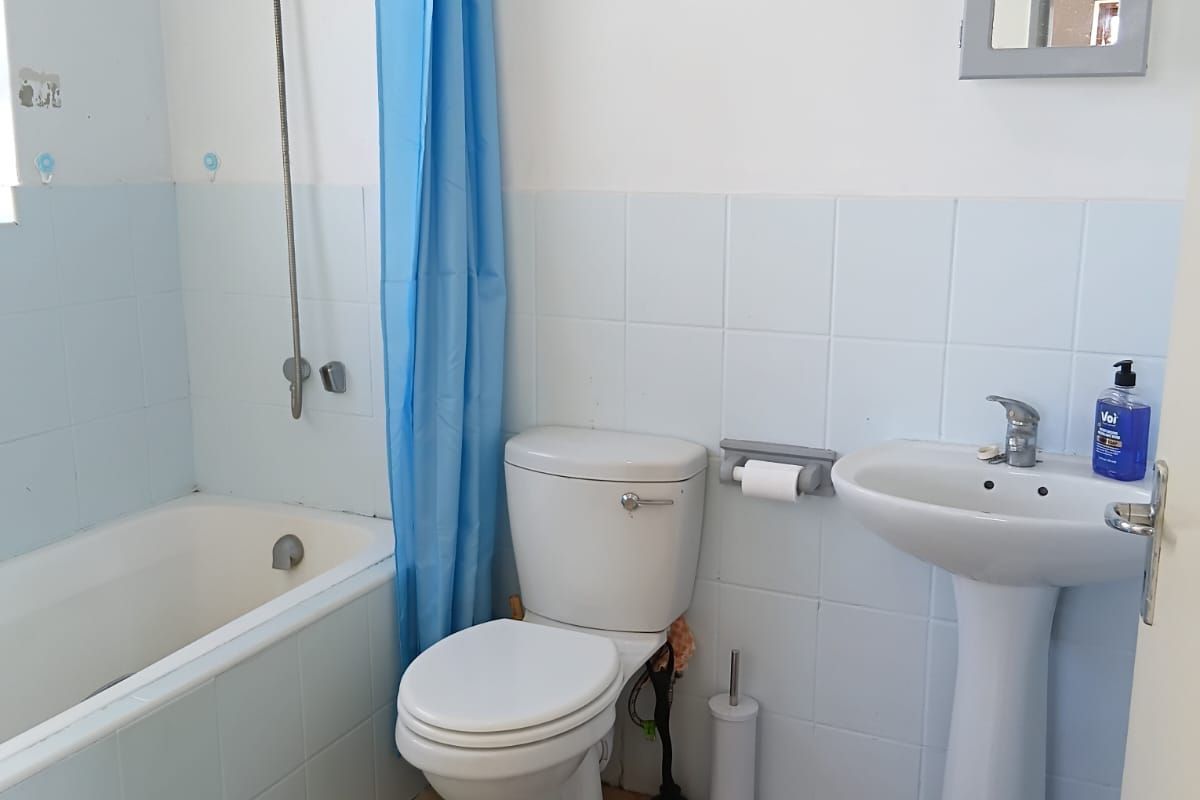 A functional bathroom featuring a bathtub with shower attachment, pedestal sink, and toilet, finished with light blue wall tiles and neutral floor tiles.