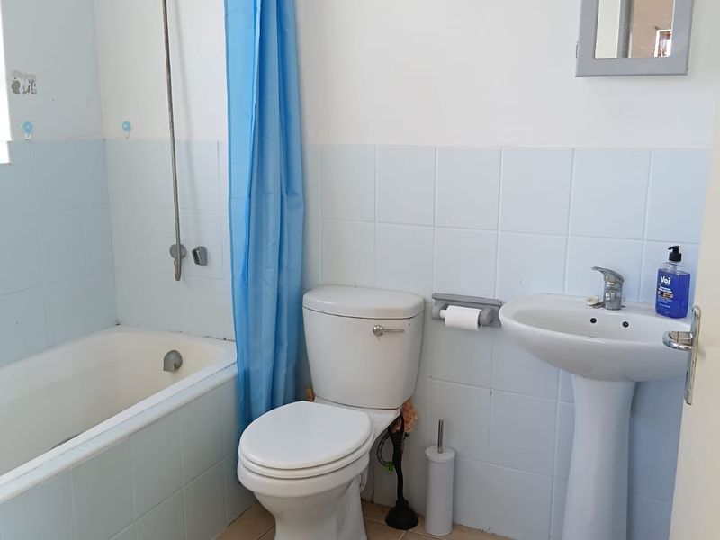 A functional bathroom featuring a bathtub with shower attachment, pedestal sink, and toilet, finished with light blue wall tiles and neutral floor tiles.