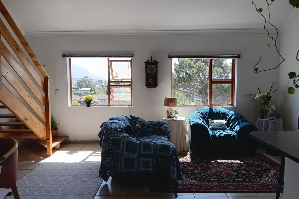 A bright living area featuring tiled floors, a wooden staircase, and large windows offering natural light and scenic views.