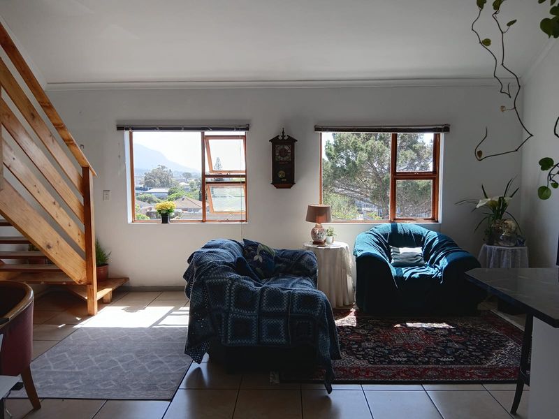 A bright living area featuring tiled floors, a wooden staircase, and large windows offering natural light and scenic views.