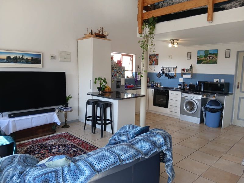 Open-plan living area featuring a functional kitchen with built-in appliances, tiled flooring, and a mezzanine level, creating a versatile and compact living space.
