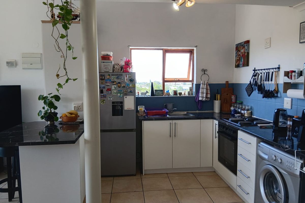 A functional kitchen featuring white cabinetry, granite countertops, built-in oven and hob, and tiled flooring, with an integrated washing machine and breakfast bar area.