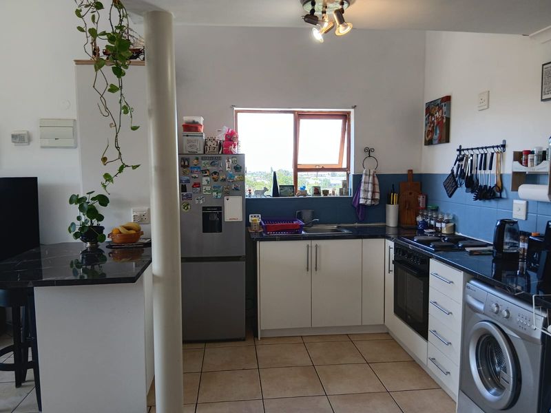 A functional kitchen featuring white cabinetry, granite countertops, built-in oven and hob, and tiled flooring, with an integrated washing machine and breakfast bar area.