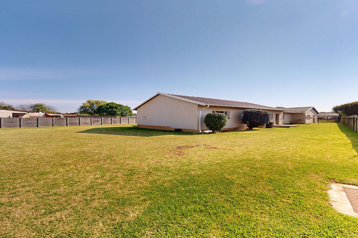 A spacious rear garden featuring a large lawn area, concrete boundary walls, and a view of the rear elevation of the house.