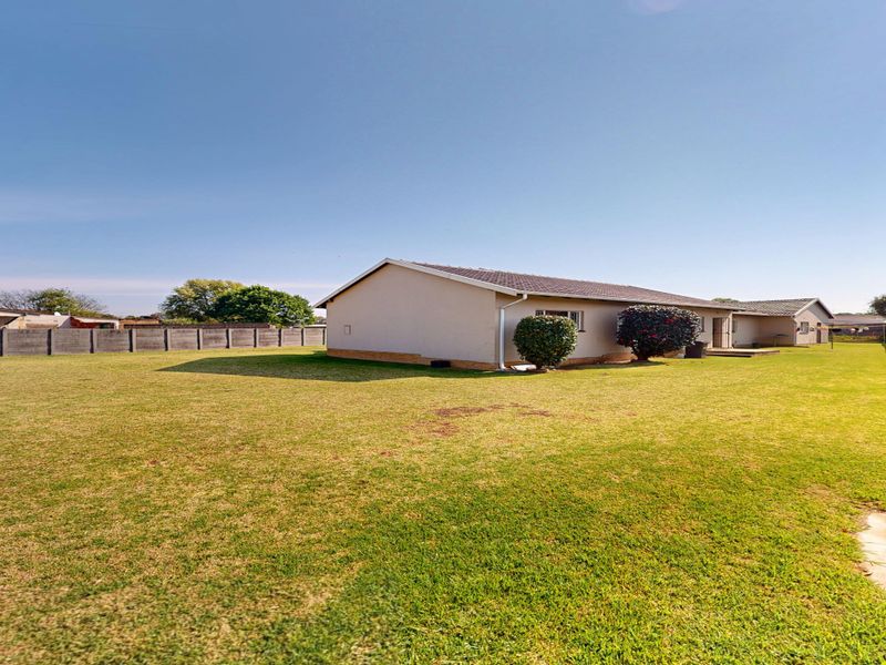 A spacious rear garden featuring a large lawn area, concrete boundary walls, and a view of the rear elevation of the house.