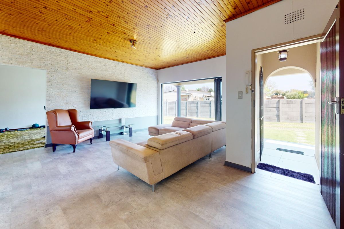 Spacious living room featuring a timber ceiling, stone-clad feature wall, and direct access to the outdoor area through a sliding glass door.