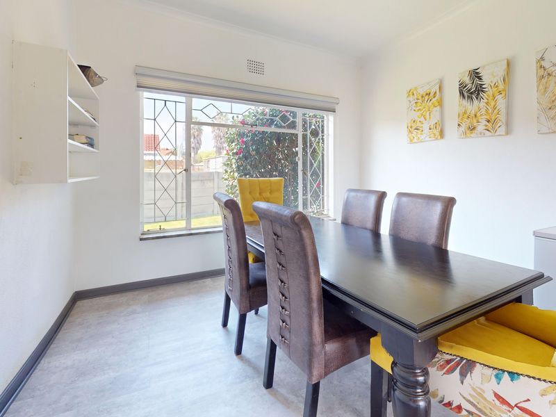 A dining room featuring neutral walls, light-toned flooring, and a large window with security bars, providing a bright and functional space for meals.