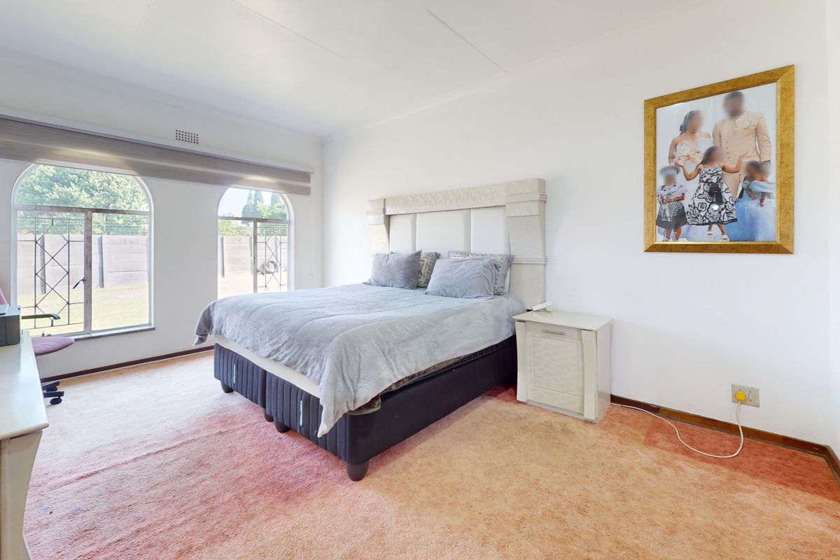 Spacious bedroom featuring arched windows with roller blinds and carpet flooring, offering a bright and functional living space.