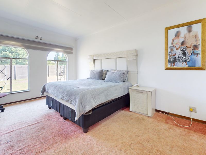 Spacious bedroom featuring arched windows with roller blinds and carpet flooring, offering a bright and functional living space.