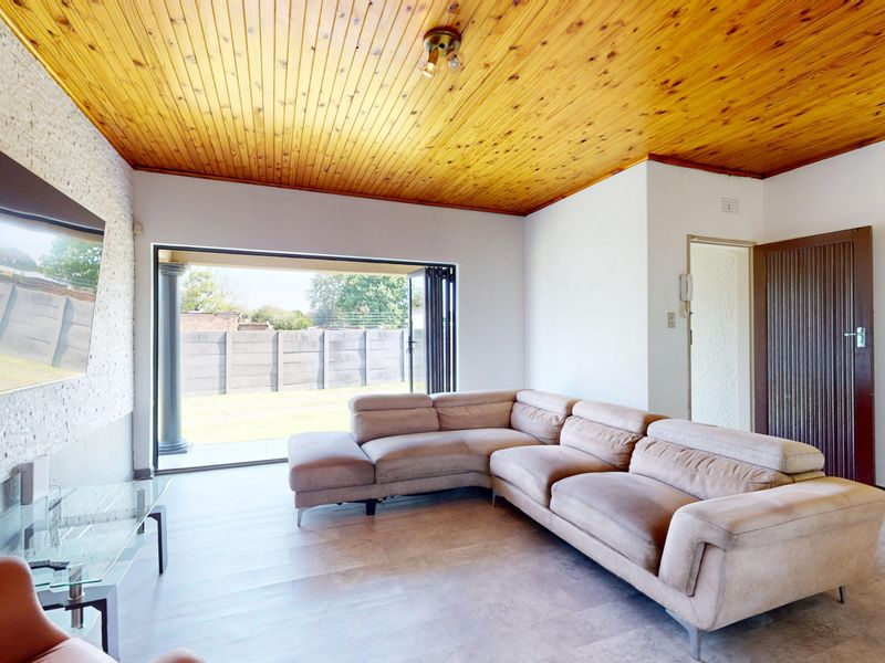Spacious living room featuring a timber tongue and groove ceiling, stone feature wall, and large stacking doors opening to the garden.