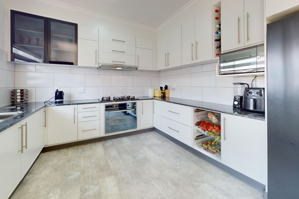 Modern kitchen featuring white cabinetry, stone countertops, built-in oven, gas hob, extractor fan, and integrated microwave with a clean, functional layout.