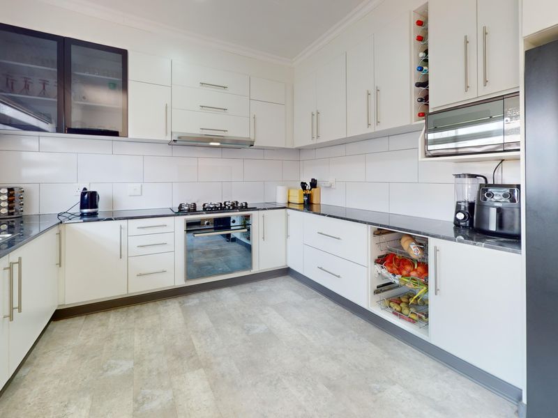 Modern kitchen featuring white cabinetry, stone countertops, built-in oven, gas hob, extractor fan, and integrated microwave with a clean, functional layout.