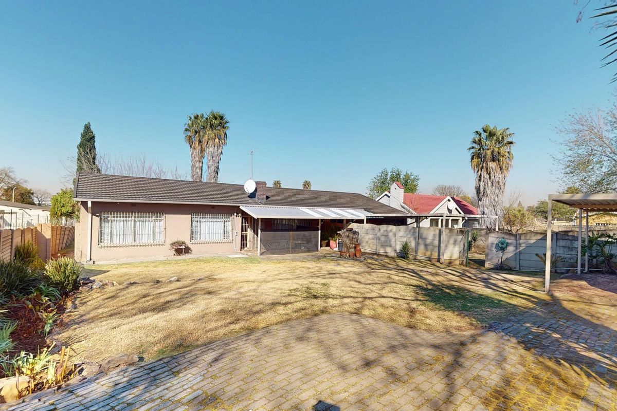 Rear view of the property featuring a covered patio, paved driveway, and a spacious garden enclosed by precast concrete walls.