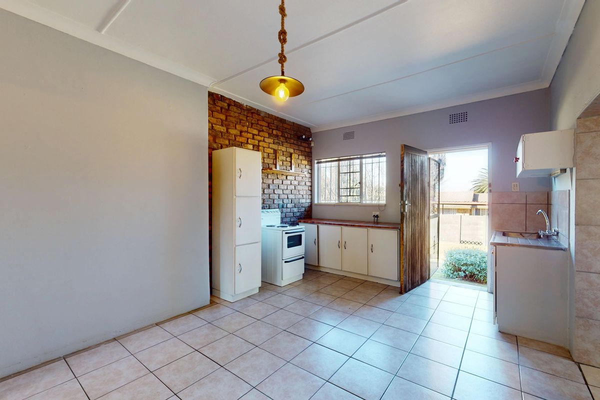 Functional kitchen featuring tiled flooring, an exposed brick feature wall, built-in cabinetry, and direct access to the rear exterior.