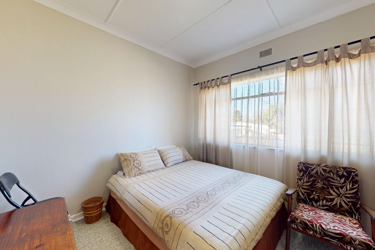 A standard bedroom featuring neutral wall finishes, a window with security bars, and a ceiling vent.