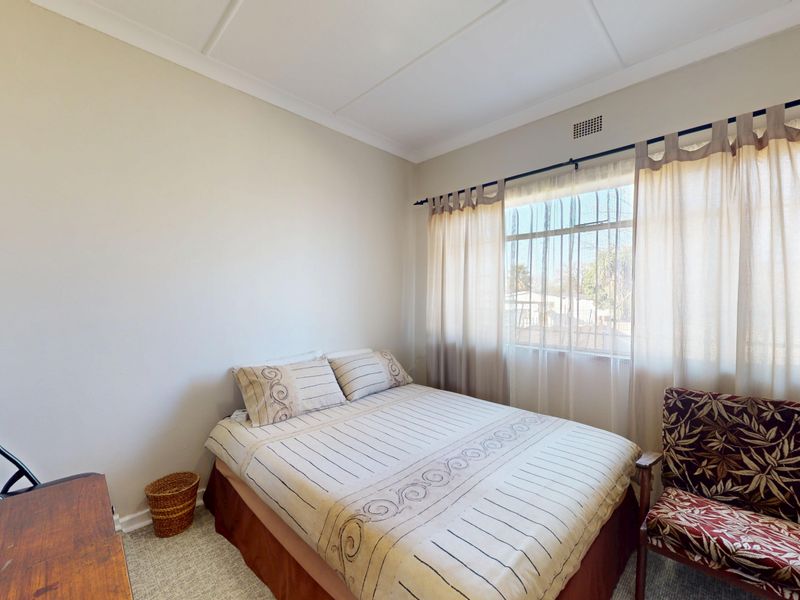 A standard bedroom featuring neutral wall finishes, a window with security bars, and a ceiling vent.